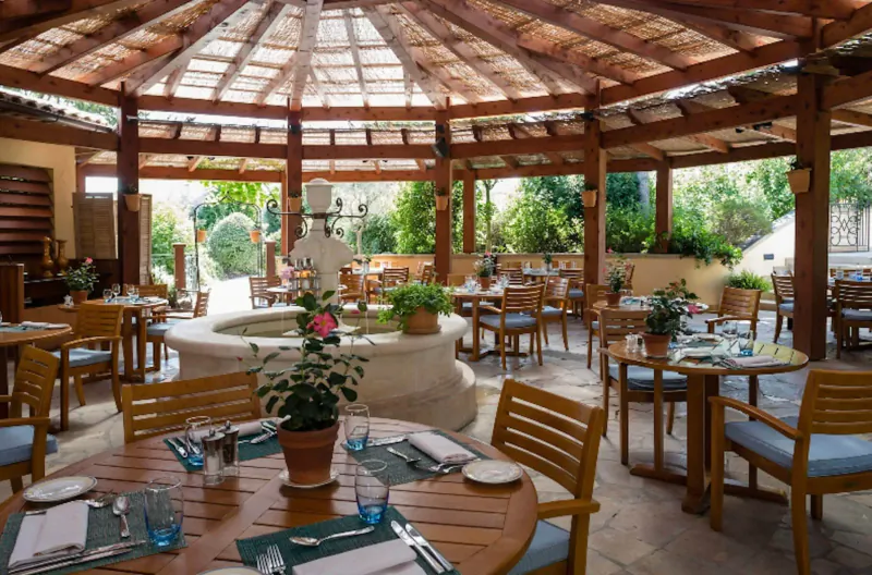 Elegant outdoor dining pavilion at Terre Blanche resort with central stone fountain, wooden tables set with flowers, Provence garden views.