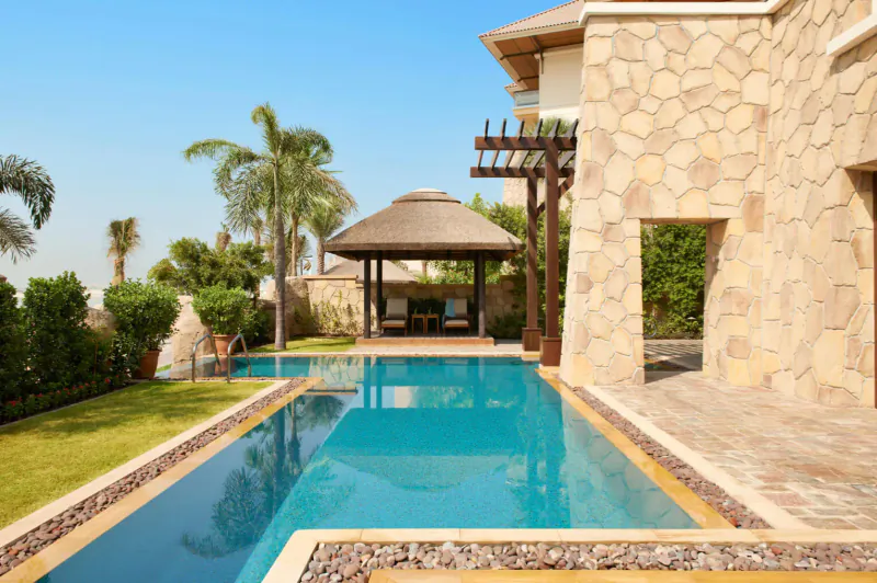 Luxury infinity pool at Sofitel Dubai The Palm resort, with stone villa, thatched pergola, palms, and blue sky.