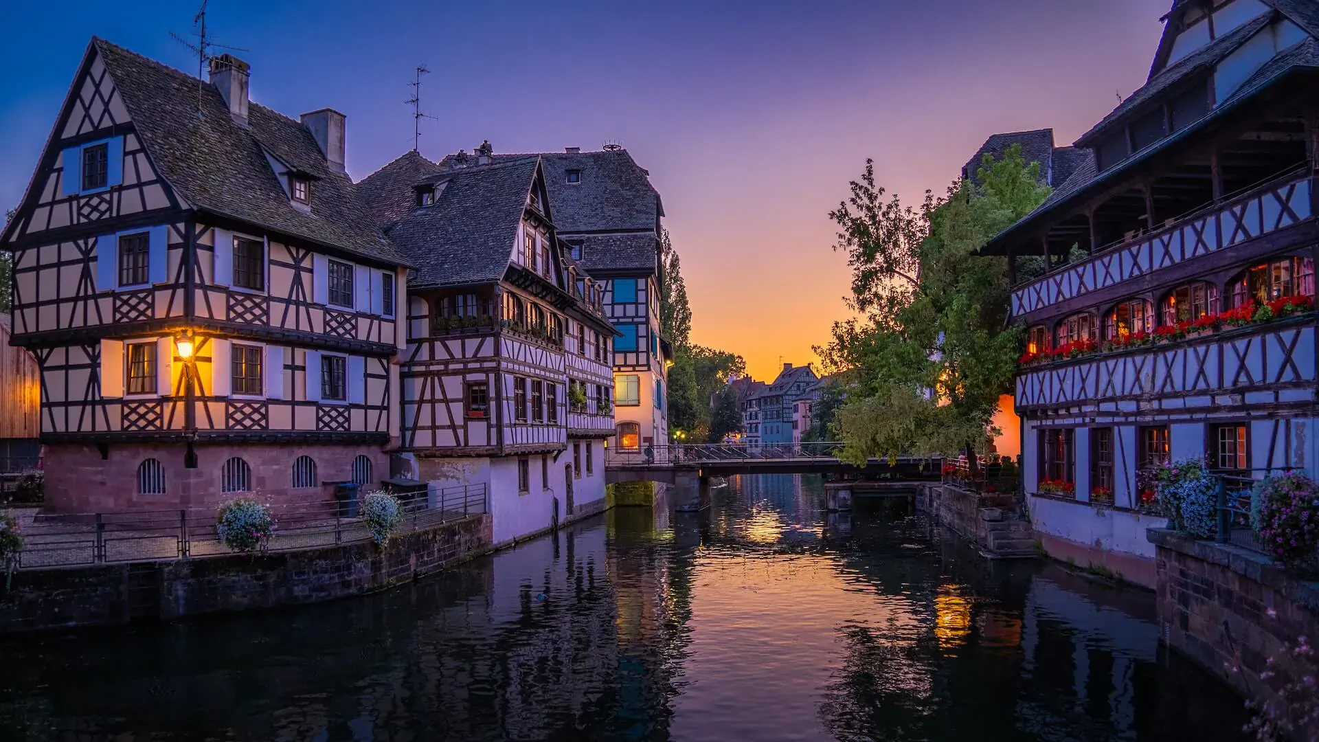 Twilight view of half-timbered houses and bridge reflecting in Rhine River, fairy-tale setting.