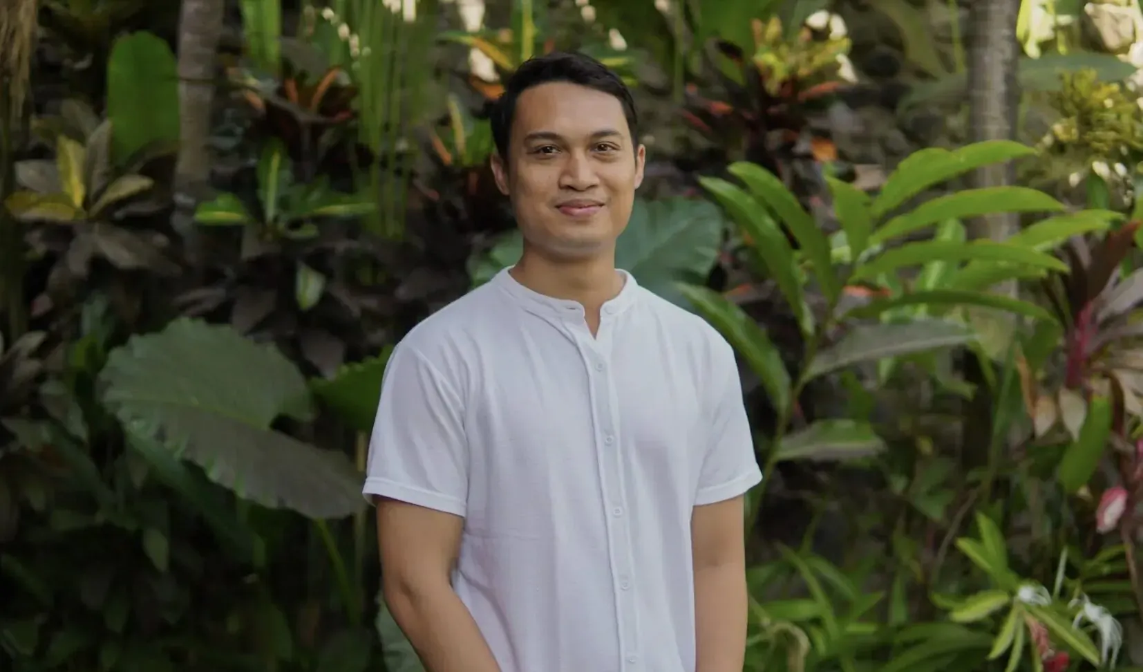 Anak Agung Ngurah Surya Darma, CFO of Gdas Bali, smiling in white shirt against lush tropical plants