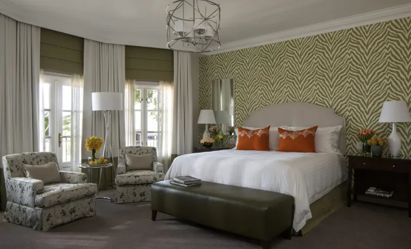 Elegant hotel bedroom at Four Seasons Westcliff, Johannesburg: king bed with orange pillows, zebra wallpaper, armchairs, lamps, flowers.
