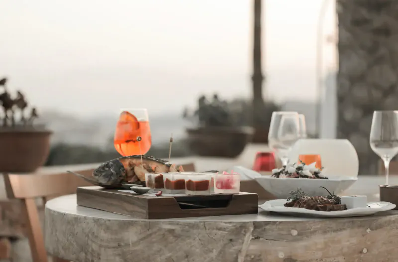 Outdoor table at Destino Pacha Ibiza with wooden charcuterie board, orange Aperol spritz, shrimp dish, and wine glasses overlooking sunset view.