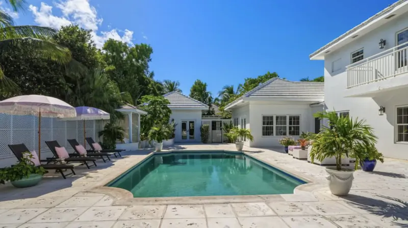 Luxury white villa with turquoise pool, pink umbrellas, lounge chairs, palms in tropical garden, Lyford Cay.