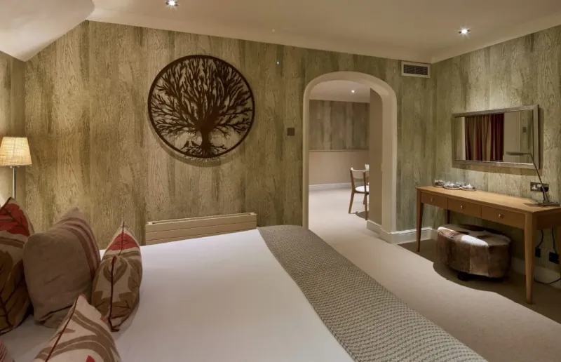 Luxury hotel bedroom with tree wall art, beige textured walls, bed with red pillows, and en-suite glimpse.