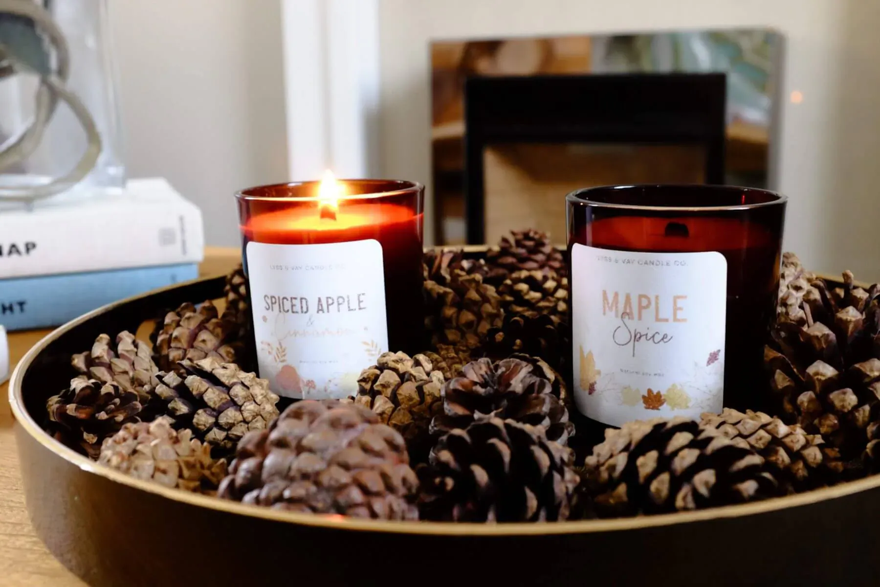 Tray of pinecones with lit 'Spiced Apple' and 'Maple Spice' candles, autumn decor on table.