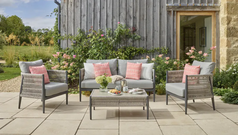 Bramblecrest premium grey wicker outdoor sofa set with pink cushions on patio, surrounded by garden and roses.