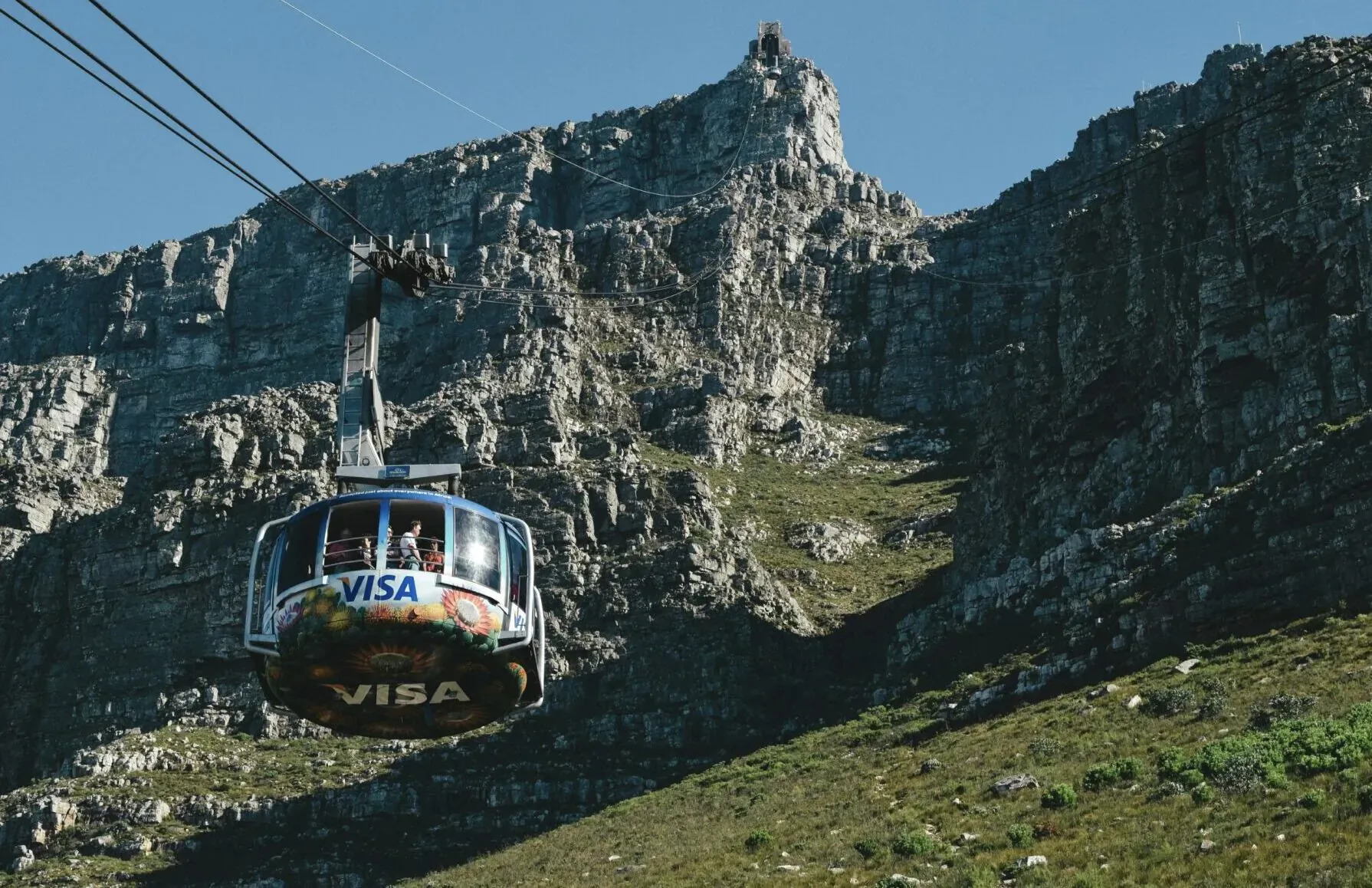 Visa-branded cable car ascending steep cliffs toward Table Mountain's peak in Cape Town.