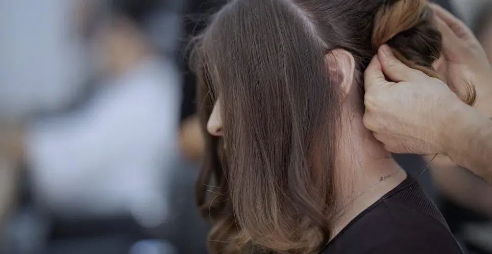 Stylist braiding woman's long brown hair in salon, sustainable hair care trend