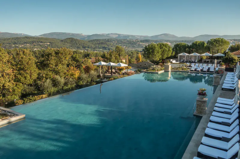 Infinity pool at Terre Blanche resort in Provence, with loungers, umbrellas, and distant hills under blue sky.