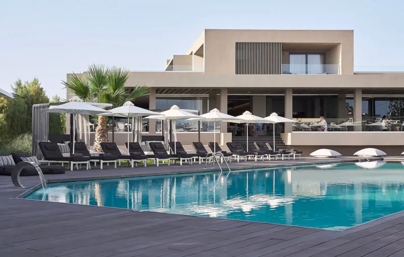 Infinity pool with loungers and umbrellas at modern Elysium Boutique Hotel in Crete, overlooking sea.