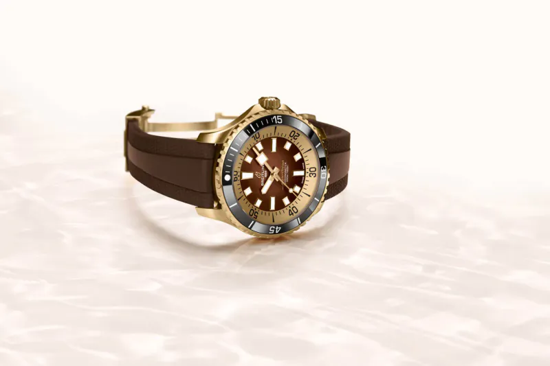 Rolex Submariner-style dive watch with gold case, brown rubber strap, and bezel on white watery surface