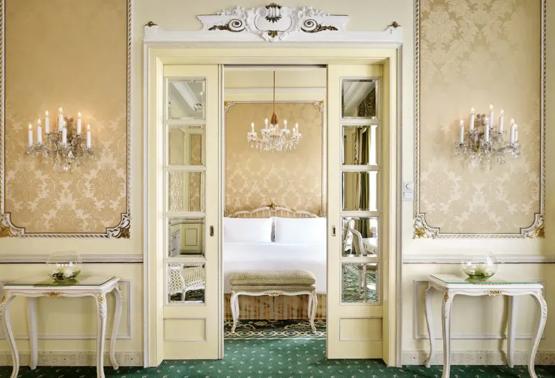 Open ornate doors to luxurious bedroom with chandelier, candelabras, and king bed at Hotel Imperial Vienna