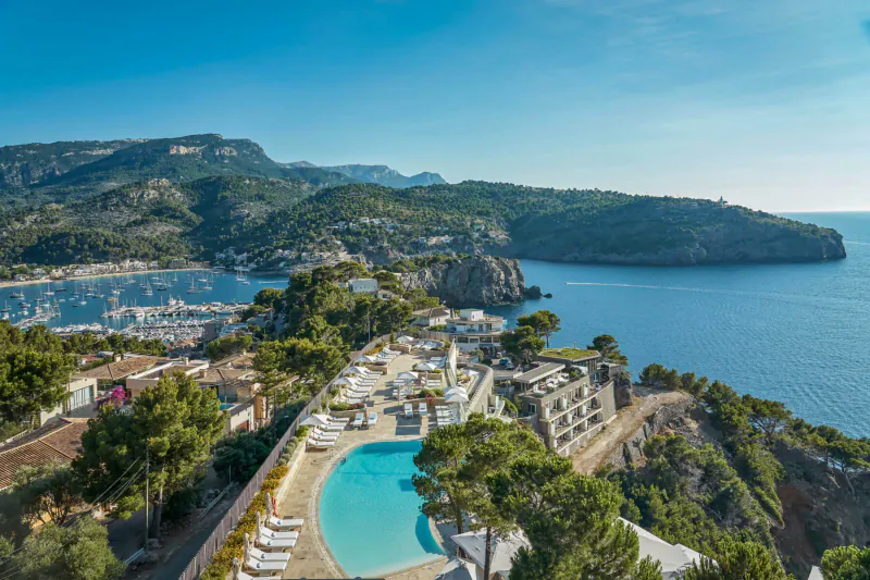 Aerial view of Jumeirah Port Söller Hotel & Spa in Mallorca: infinity pool, sunbeds, marina, sea, and mountains.