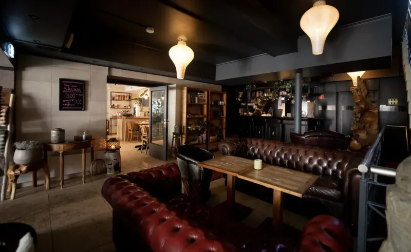 Cozy lounge interior with tufted leather sofas, wooden table, pendant lamps, and plants in a sustainable tropical hotel setting.
