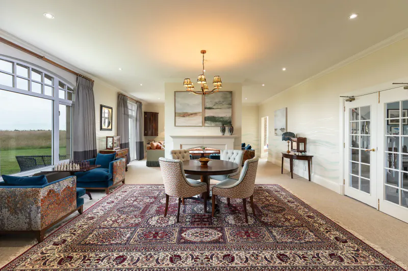 Elegant luxury manor home living room with round dining table, velvet chairs, ornate rug, chandelier, and landscape art.