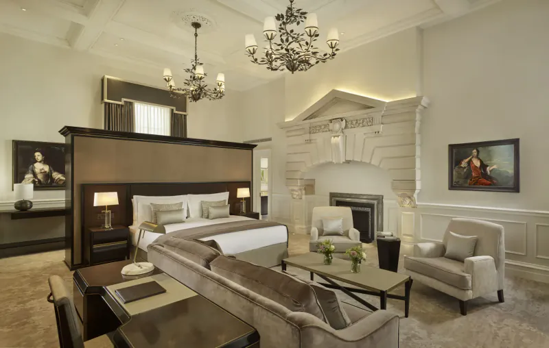 Elegant luxury hotel suite at The Langley with king bed, chandelier, fireplace, armchairs, and paintings.
