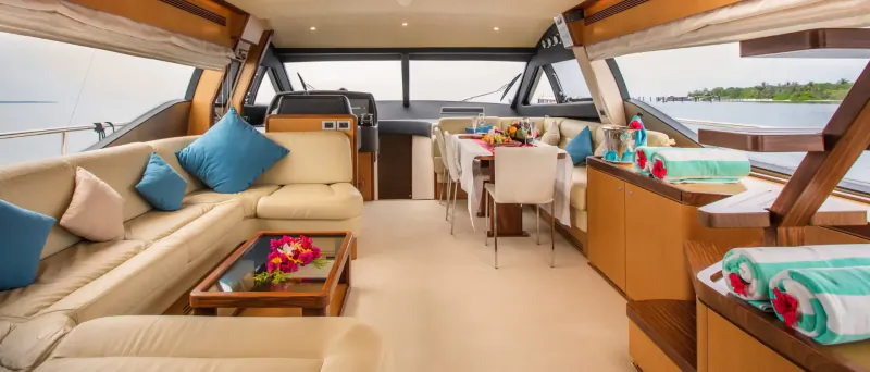 Spacious interior of Hideaway Majesty luxury yacht with cream sofas, turquoise cushions, dining table, and ocean view.
