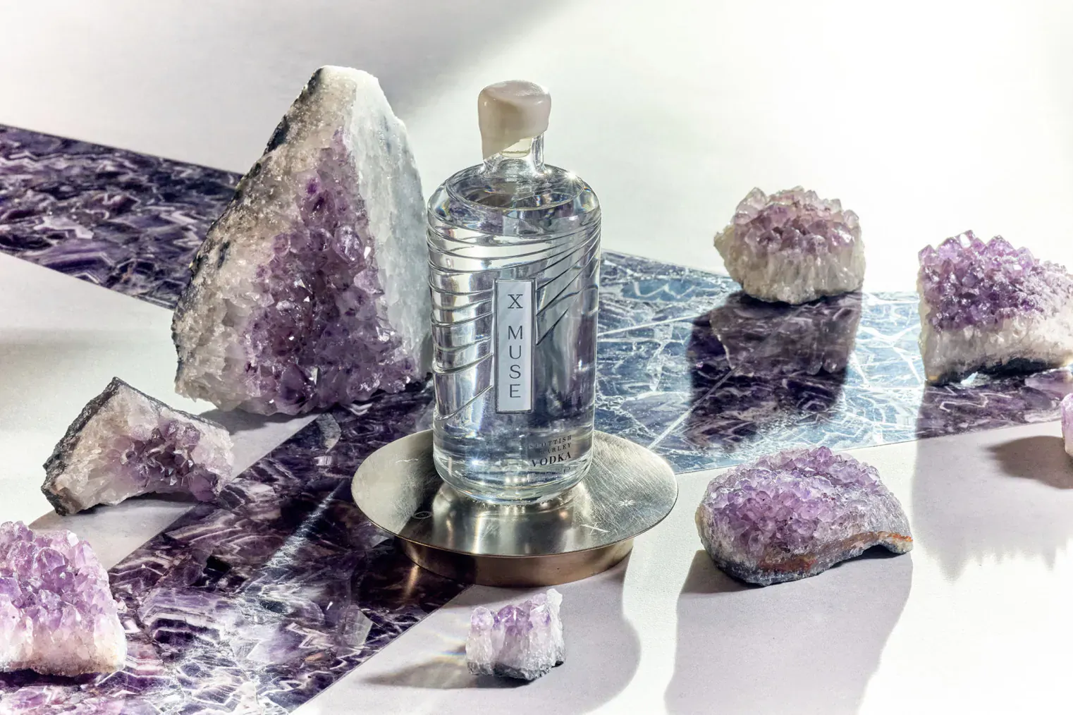 X MUSE vodka bottle on brass stand amid amethyst crystals for National Vodka Day