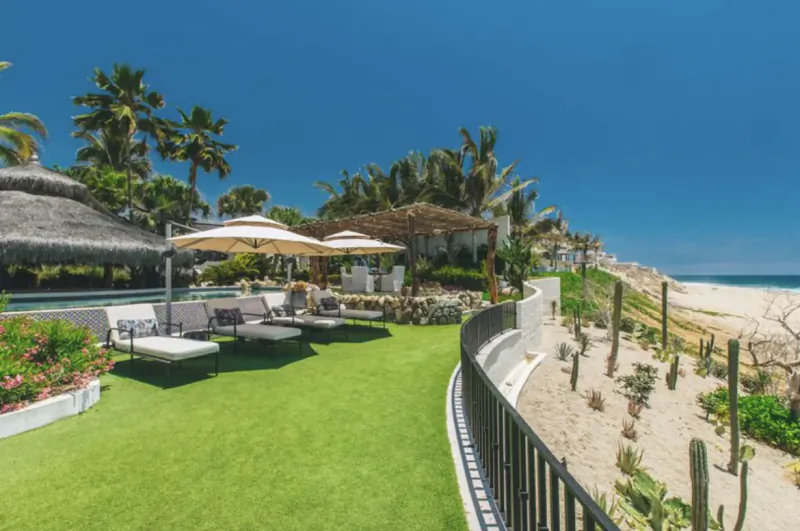 Luxury beachfront resort pool with lounge chairs, umbrellas, palms, and ocean view under blue sky