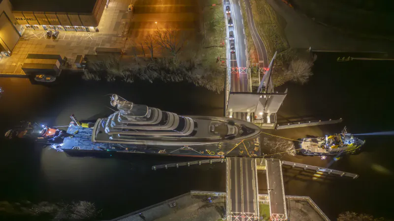 Aerial night view of a large multi-deck yacht moored at a lit lock gate with bridge and tugboats.