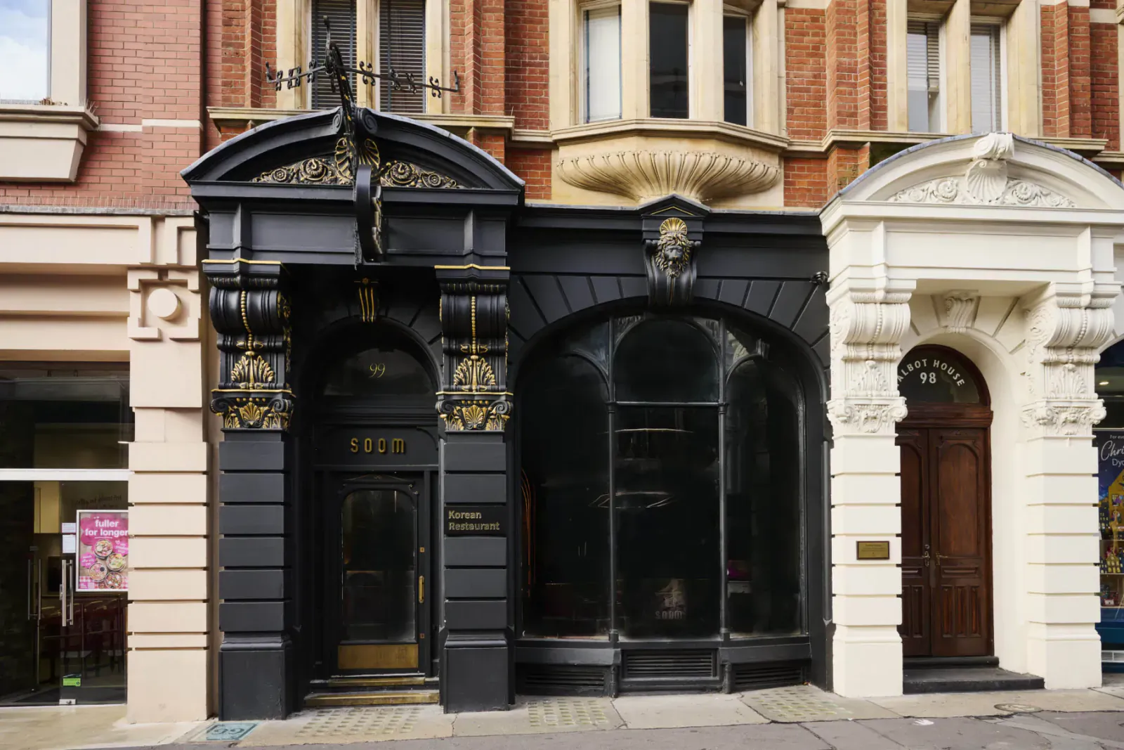 Ornate black 'TEP' entrance flanked by white arched doors on brick building facade, with large shop windows.