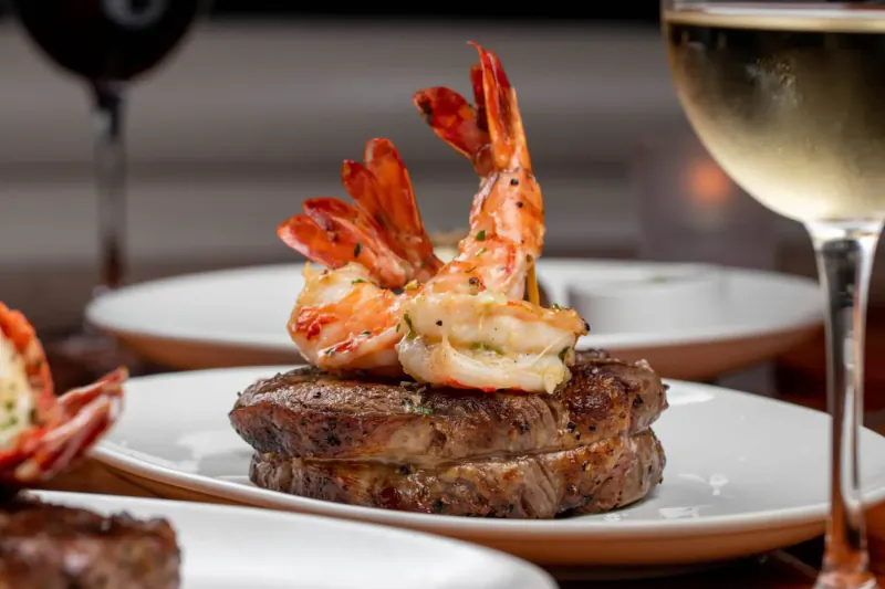 Seared steak topped with garlic shrimp on white plate, garnished with wine glasses at STK restaurant