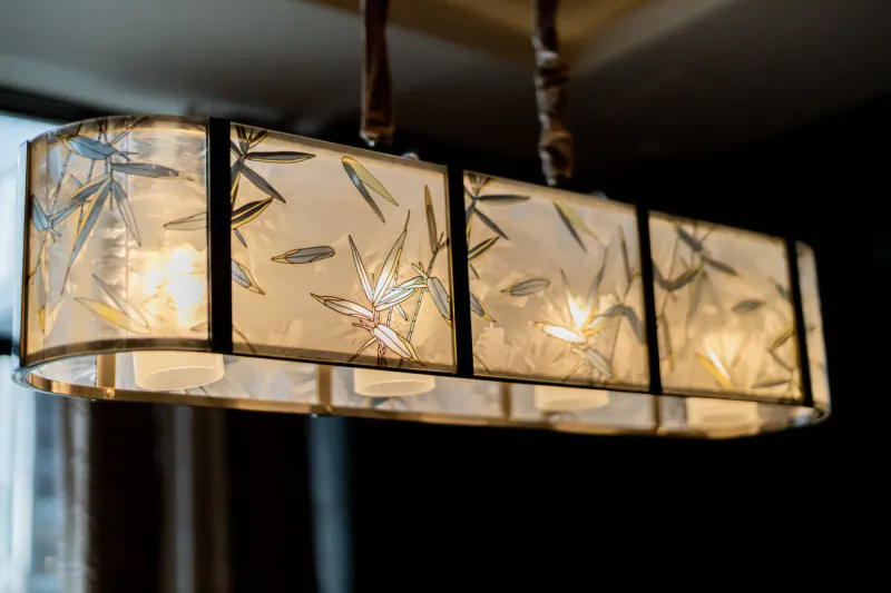 Elegant rectangular frosted glass chandelier with leaf motifs, glowing warmly from ceiling.