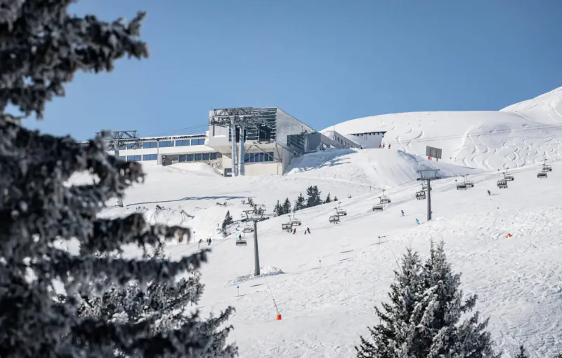 Snowy ski resort in St Anton am Arlberg with modern buildings, ski lifts, and pistes under blue sky