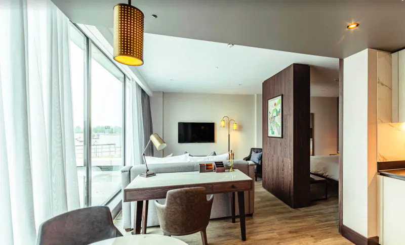 Luxury apartment living room at The Fellows House Cambridge with sofa, dining table, TV, lamps, and city view.