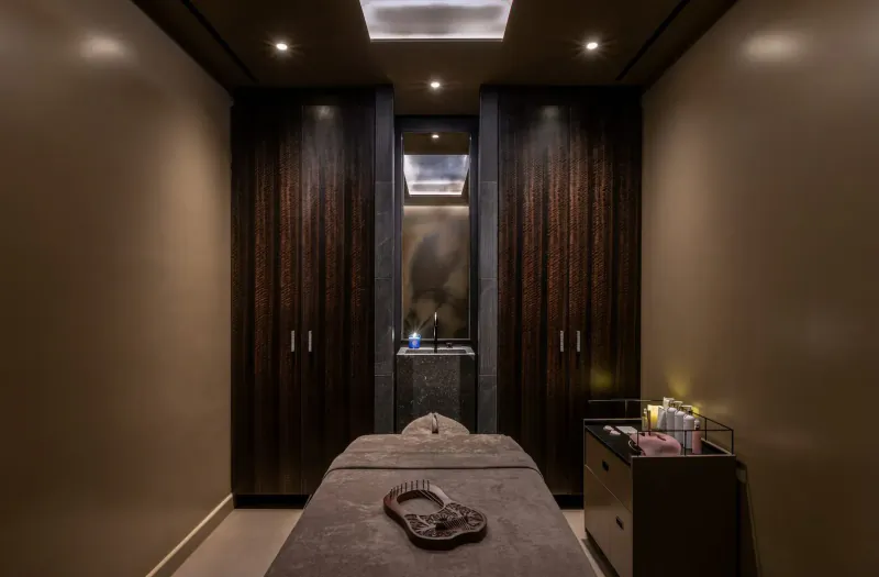 Luxurious spa treatment room with massage table, wooden cabinets, ambient lighting, and vanity.