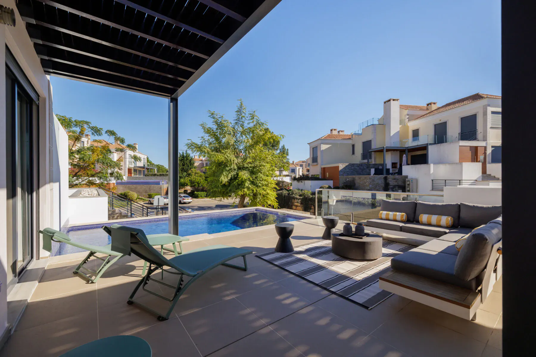 Sunny outdoor pool terrace at Vale do Lobo resort, Portugal, with lounge chairs, modern seating, and white villas.