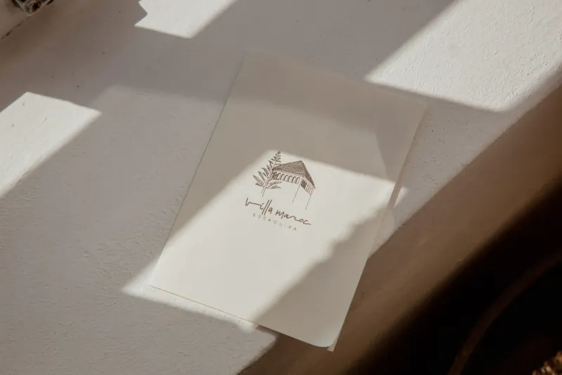 Villa Maroc invitation card on table in soft light, featuring elegant house sketch and 'Villa Maroc' text.