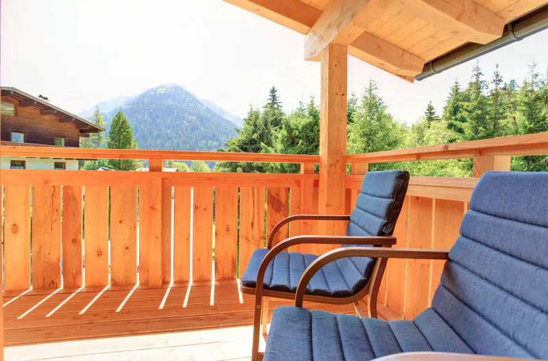 Wooden balcony with two blue cushioned chairs overlooking mountains and pine trees at Hotel Kösslerhof.