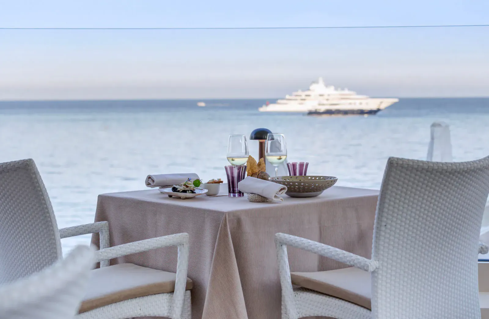 Elegant outdoor table set for two with champagne, overlooking Monaco sea and luxury yacht from Michelin restaurant.