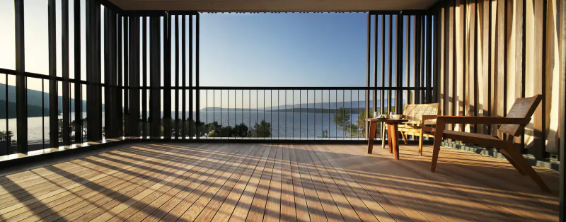 Spacious wooden terrace at Maslina Resort spa with wooden chairs overlooking serene lake and hills at sunset