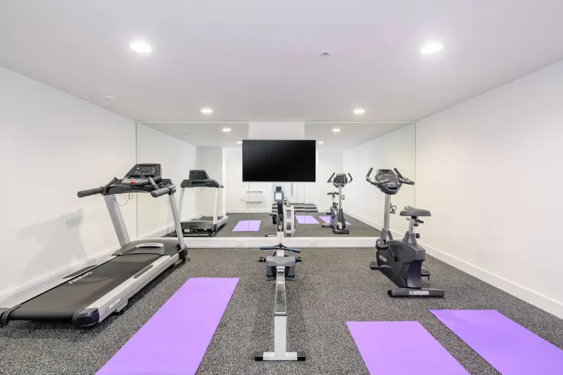 Modern gym with treadmill, exercise bikes, rowing machine, purple yoga mats, mirrors, and TV in Woolacombe Bay resort