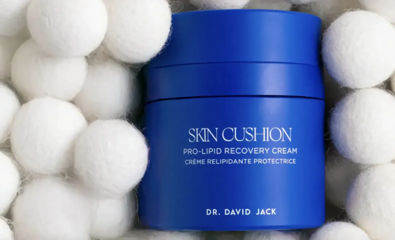 Dr. David Jack's Skin Cushion Pro-Lip Recovery Cream in blue jar surrounded by white pom poms. Labels: 'SKIN CUSHION', 'PRO-LIPID RECOVERY CREAM', 'CRÈME RÉLIPIDANTE PROTECTRICE'.