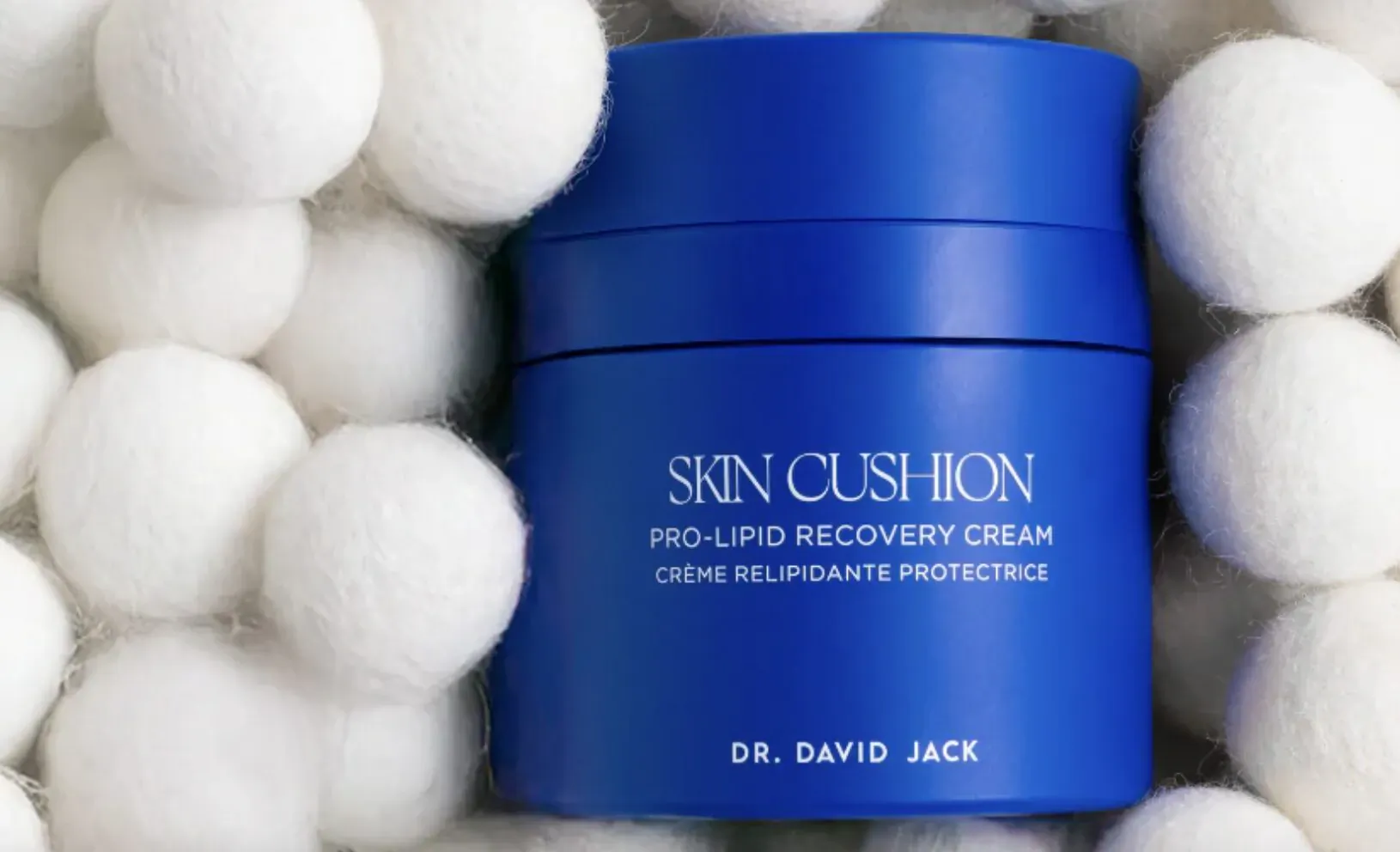 Dr. David Jack's Skin Cushion Pro-Lip Recovery Cream in blue jar surrounded by white pom poms. Labels: 'SKIN CUSHION', 'PRO-LIPID RECOVERY CREAM', 'CRÈME RÉLIPIDANTE PROTECTRICE'.