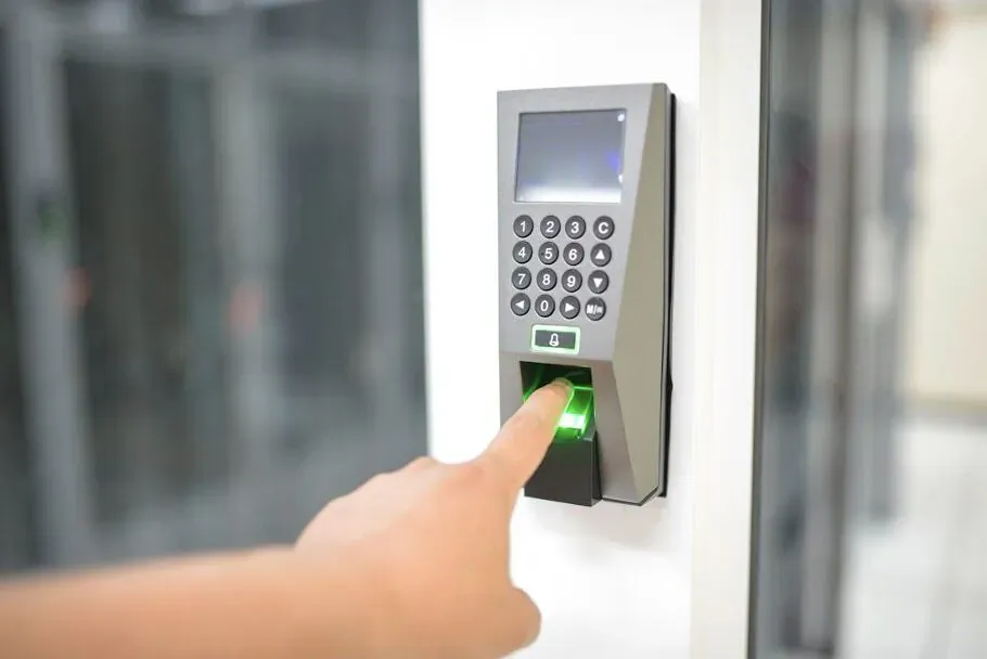 Hand scanning fingerprint on glowing green biometric keypad beside glass door for home security