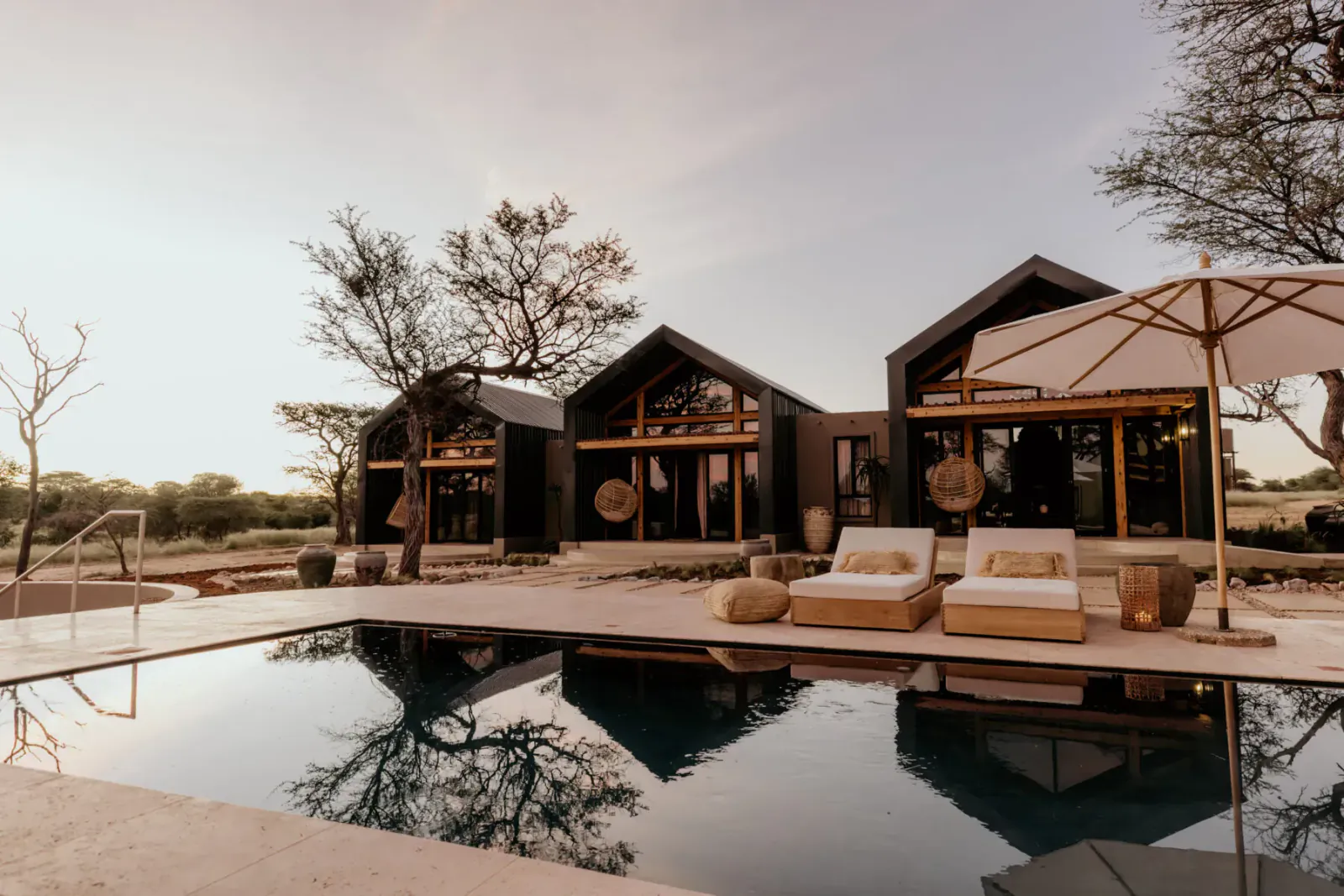Modern luxury villas with lounge chairs by infinity pool in Namibia savanna wilderness, sunset sky.