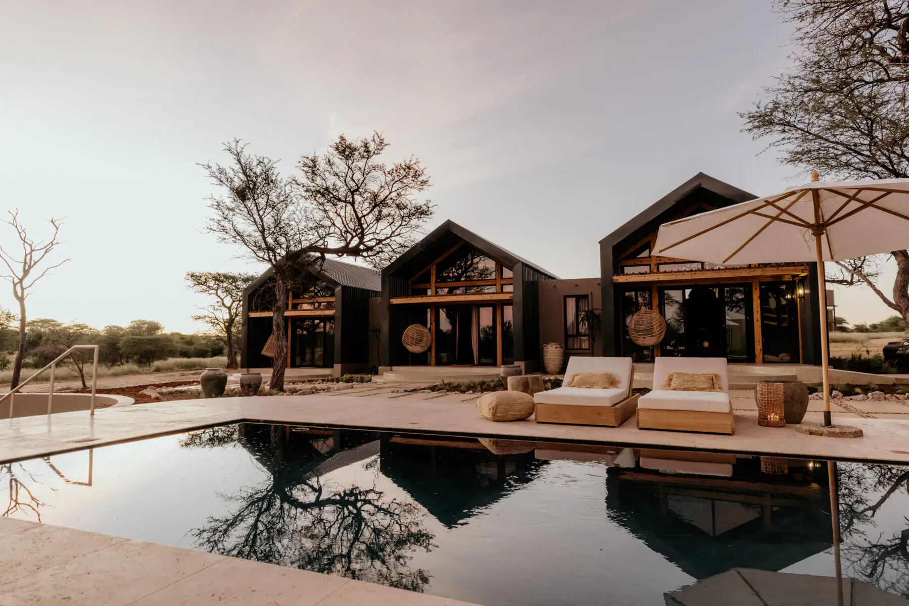 Modern luxury villas with lounge chairs by infinity pool in Namibia savanna wilderness, sunset sky.