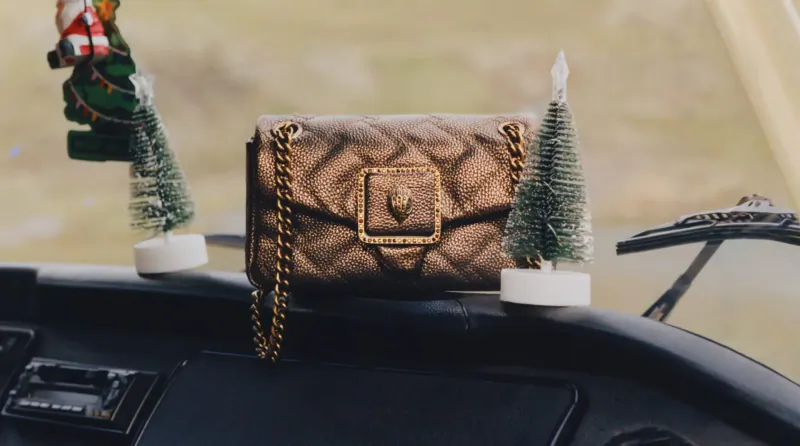 Kurt Geiger quilted chain-strap handbag on car dashboard with mini Christmas trees and Santa ornament, holiday vibe.