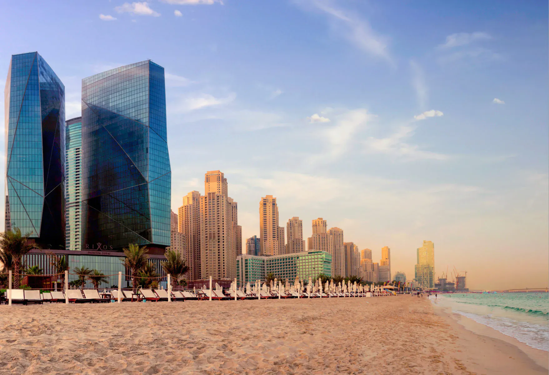 Rixos Premium Dubai: modern skyscrapers line sandy beach with umbrellas at JBR, sunset sky