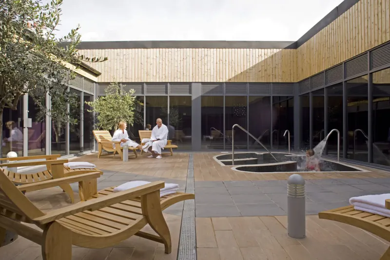 Outdoor spa courtyard at Bluestone National Park Resort with hot tub, wooden loungers, guests in robes relaxing.