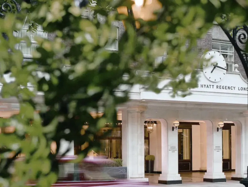 Hyatt Regency London entrance framed by lush green foliage, clock arch, and festive lighting