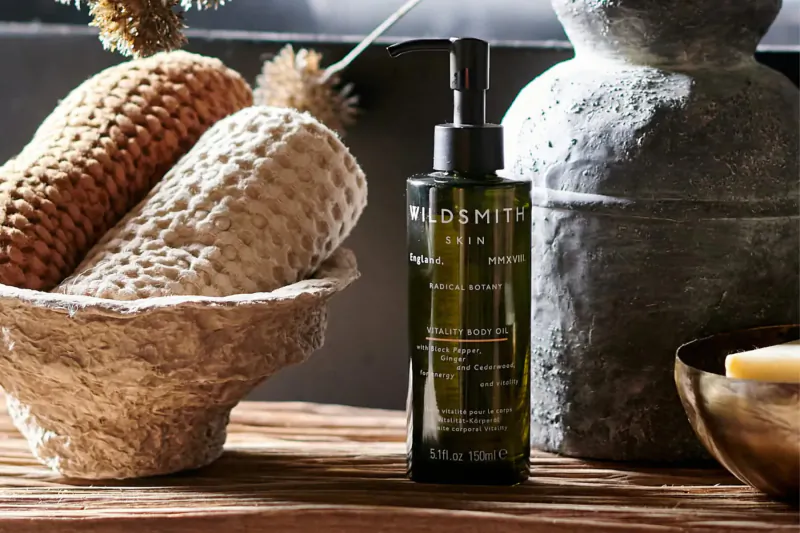 Wildsmith Skin Intensive Serum bottle on wooden surface with knitted poufs, vases, and soap dish.