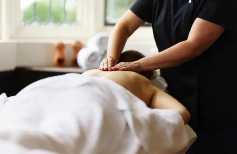 Massage therapist applying pressure to client's back on table in luxurious spa room with window.