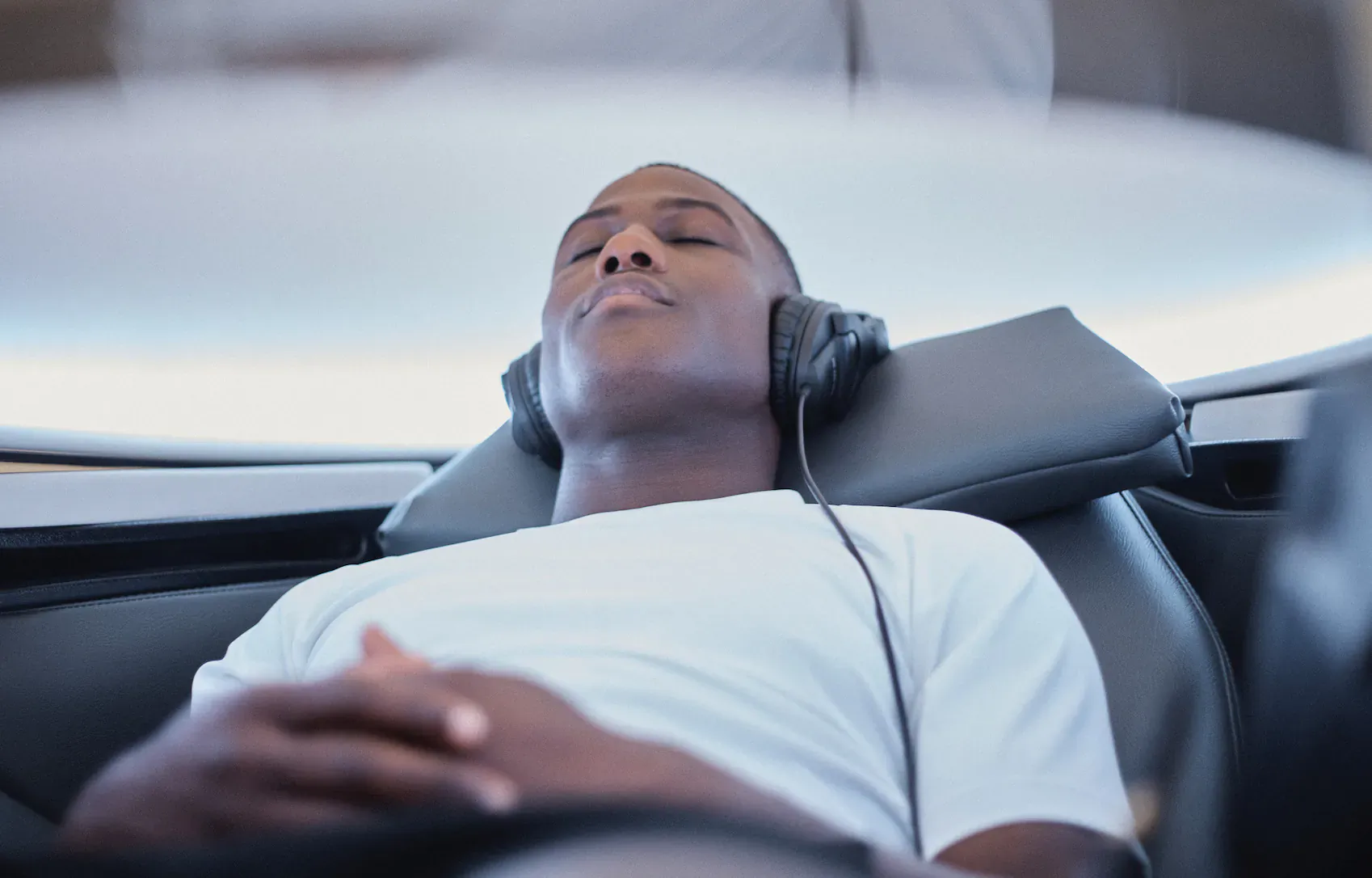 Black man reclining with eyes closed and headphones on, relaxing in plush seat at Re:place recovery studio