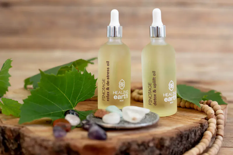 Two glass dropper bottles of Healing Earth Rose Geranium and Patchouli essential oils on wooden base with green leaves and crystals.