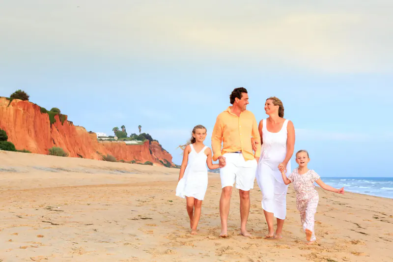 Family of four walking on Vale do Lobo beach with red cliffs and ocean backdrop
